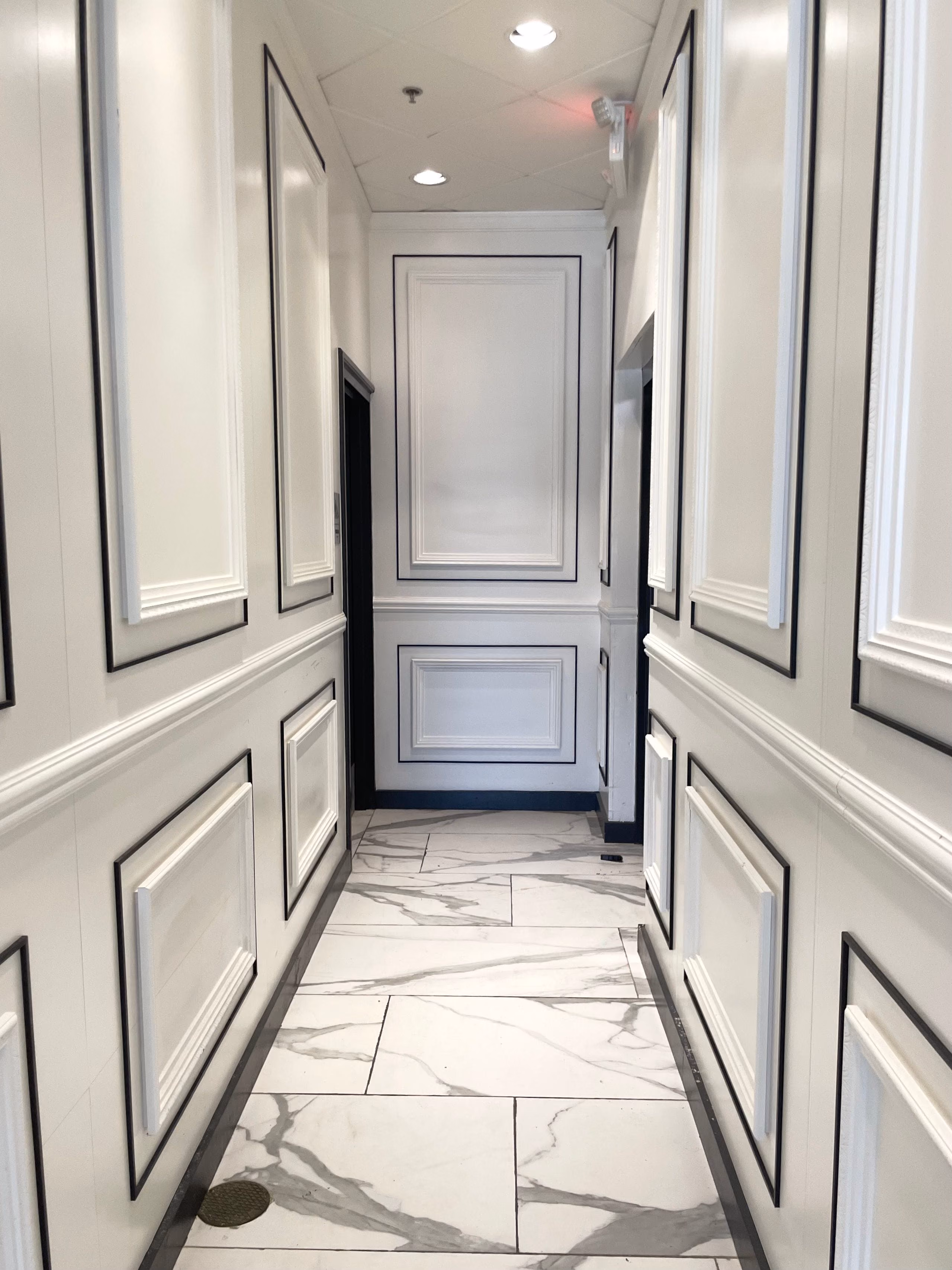 White corridor lined with raised wall panel mouldings and a marble-look tiled floor