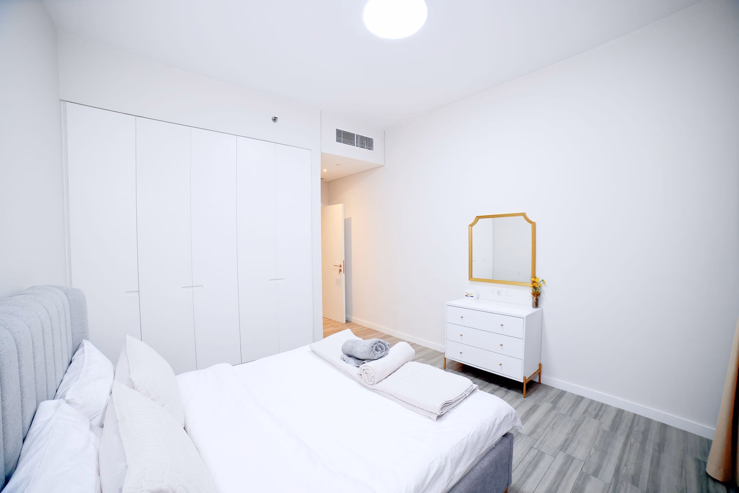 Clean white apartment bedroom with built-in wardrobes, grey plank floor and dresser
