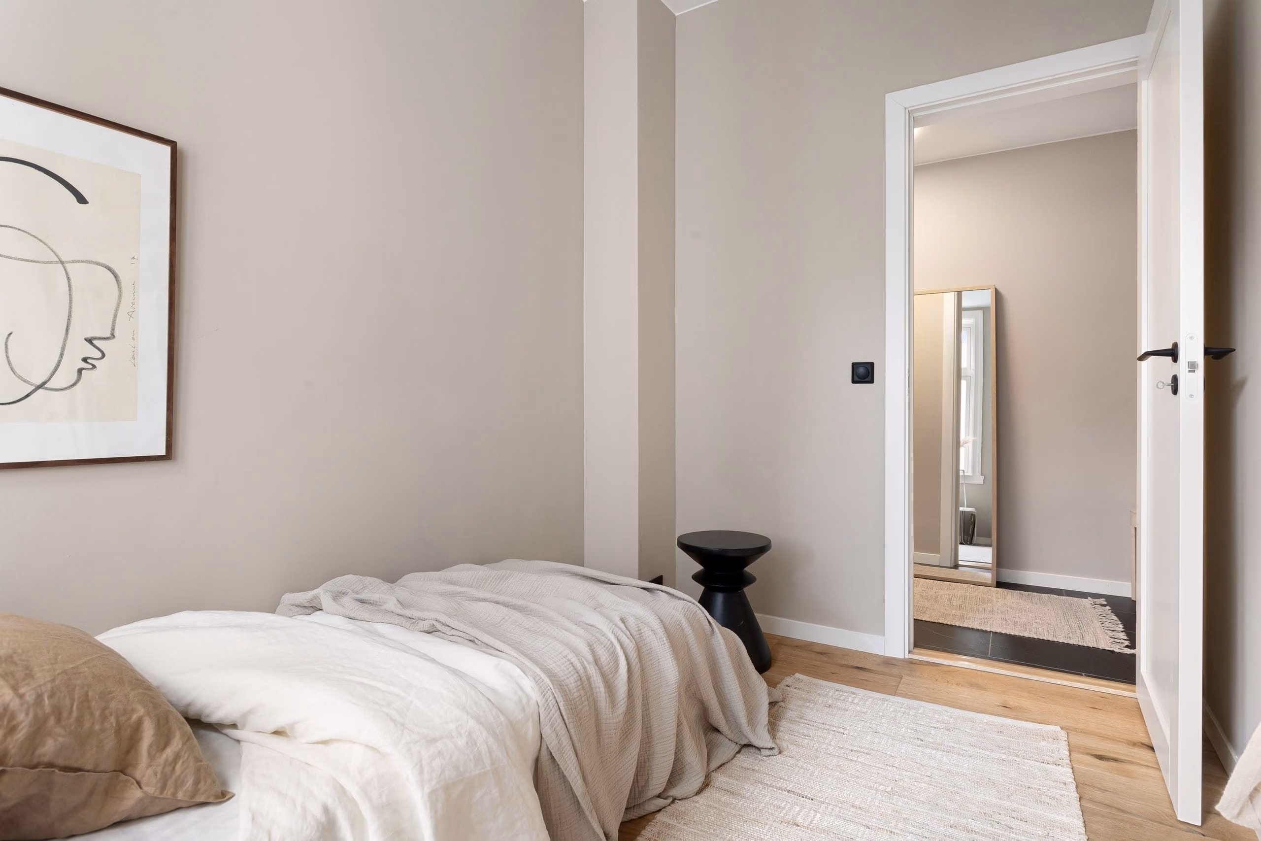 Minimalist bedroom with smooth greige painted walls, linen bedding and open door