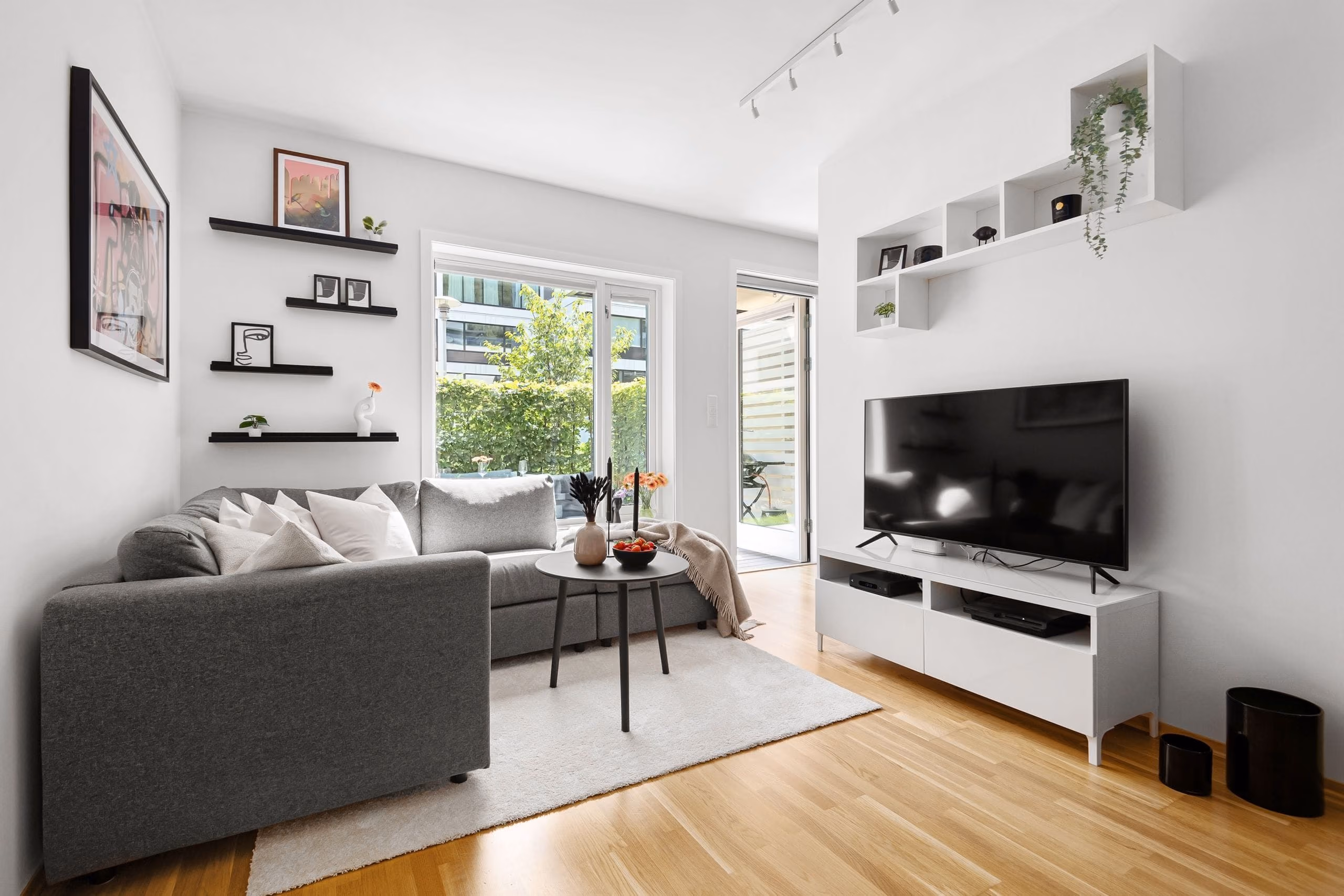 Bright living room with white walls, grey sofa, wall shelves and oak floor