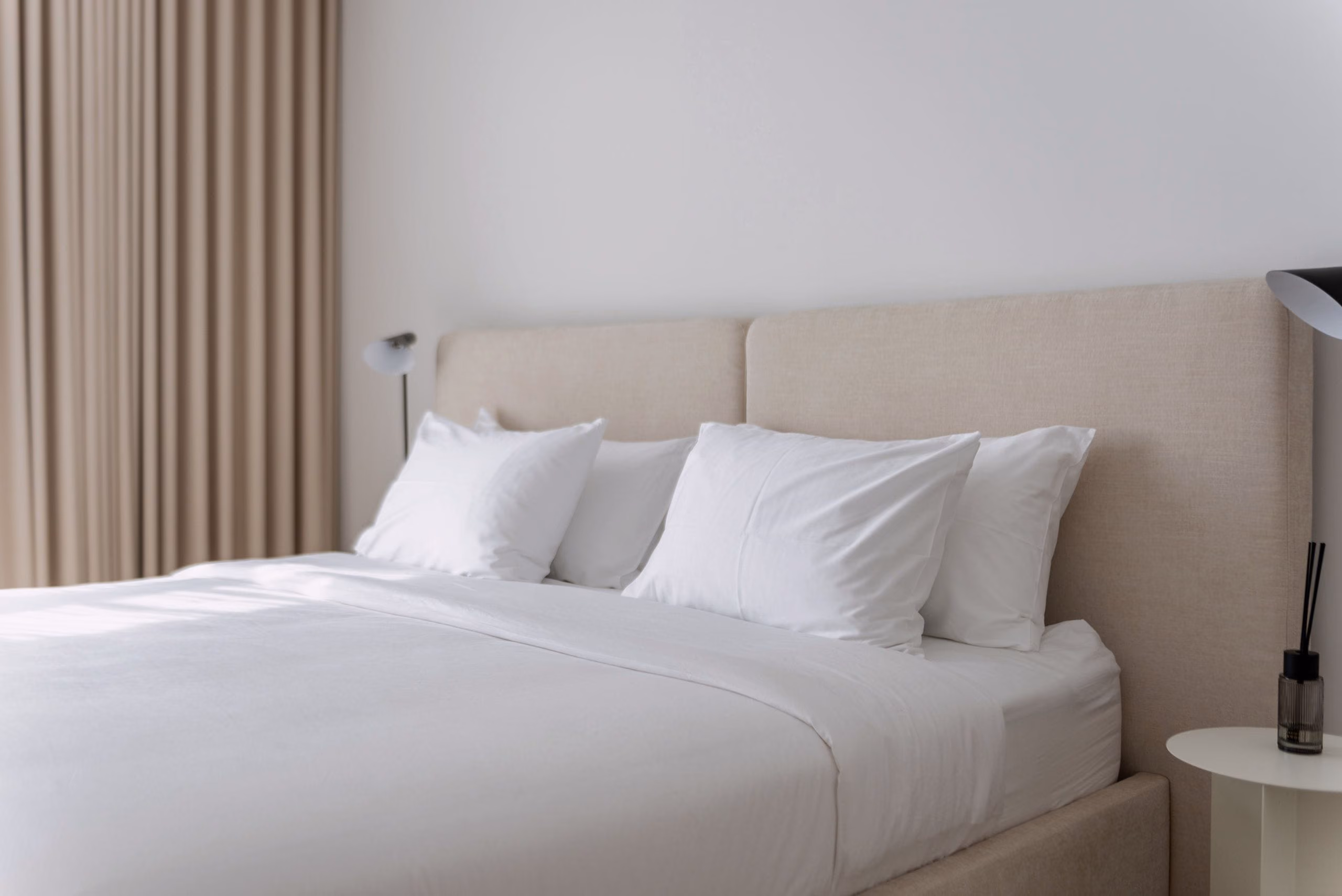 Calm bedroom with upholstered headboard, crisp white bedding and floor-length beige curtains