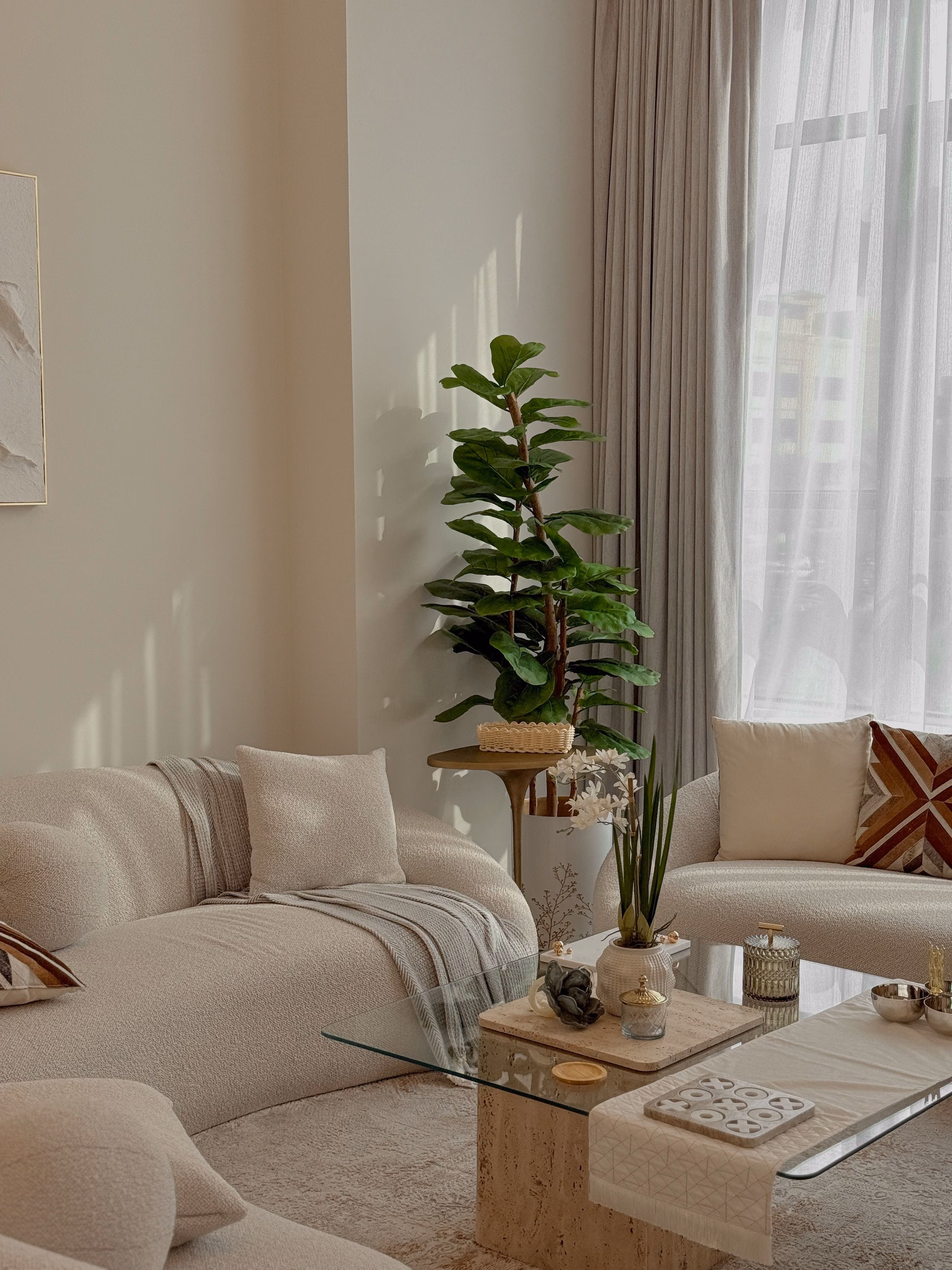 Furnished living room with cream sofas, sheer curtains, indoor plants and soft daylight