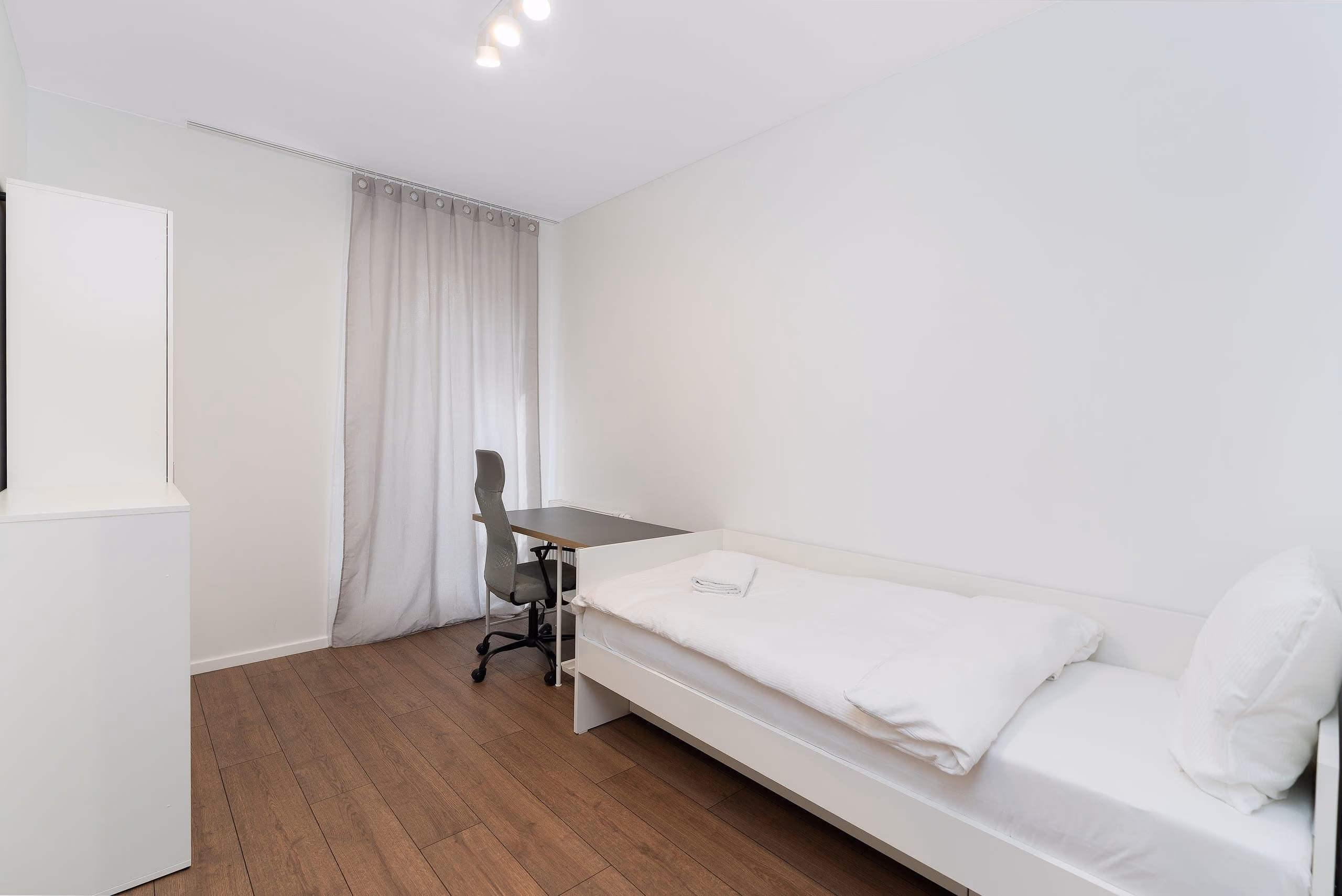White room with curtains hung from a concealed ceiling recess and plank flooring
