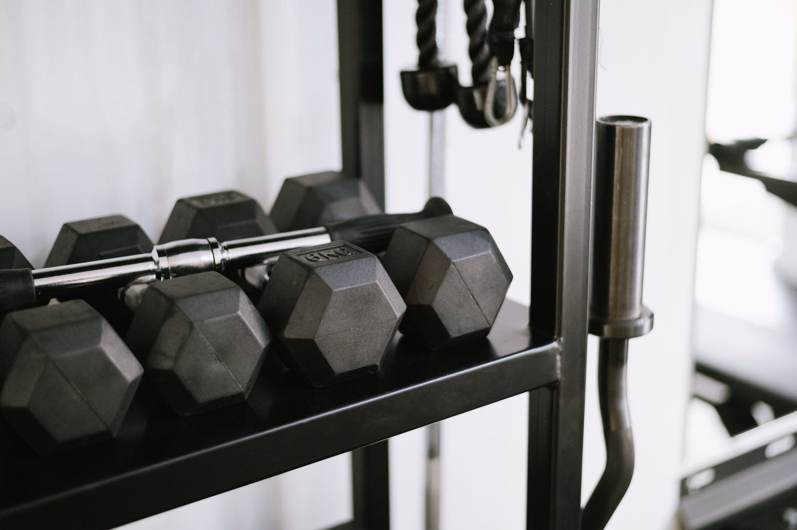 Black hexagonal dumbbells on a metal rack against a bright white wall