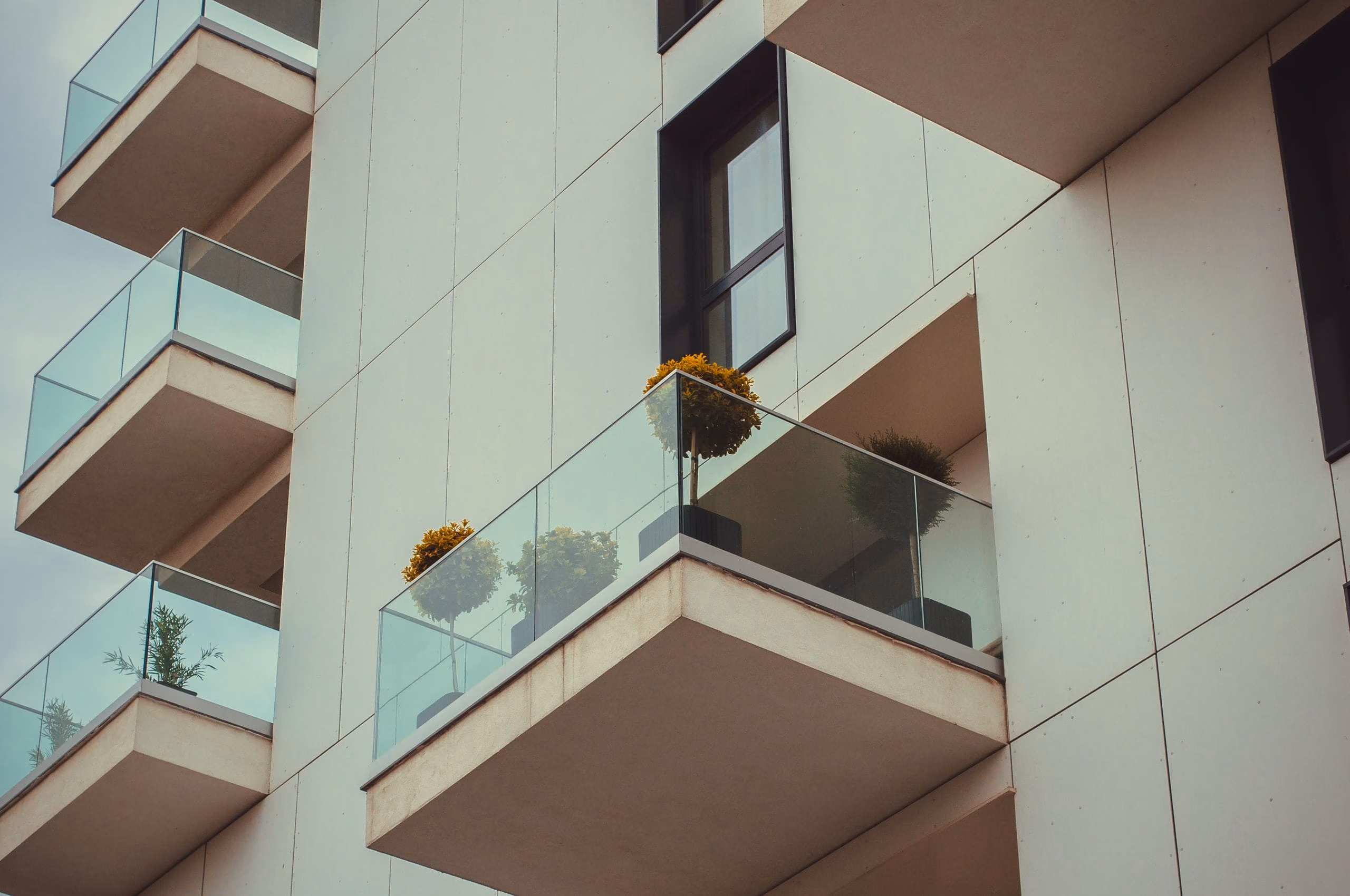 Modern building facade with frameless glass balconies and potted plants