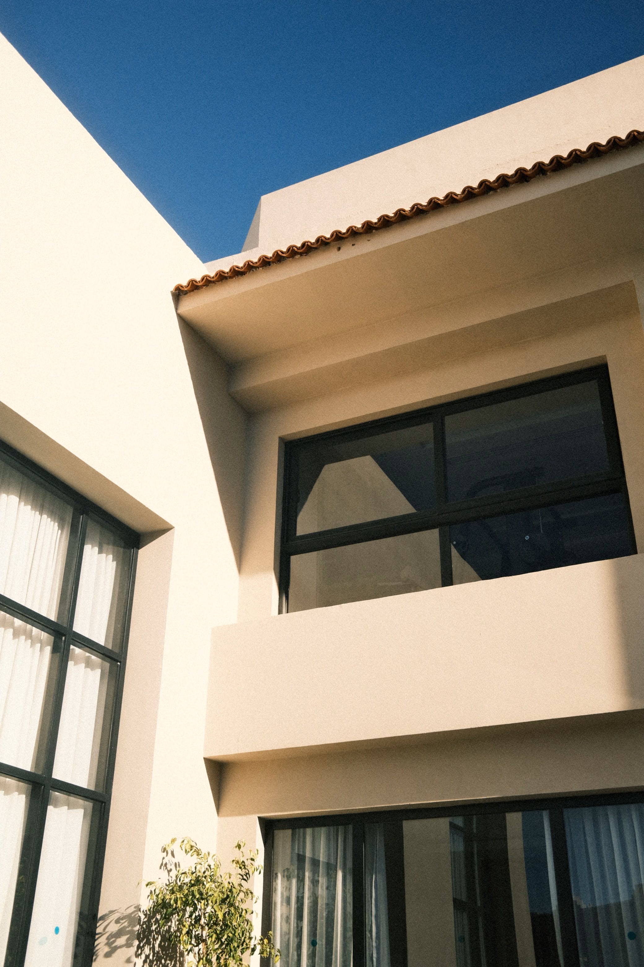 Close view of a cream rendered facade with dark window frames under blue sky