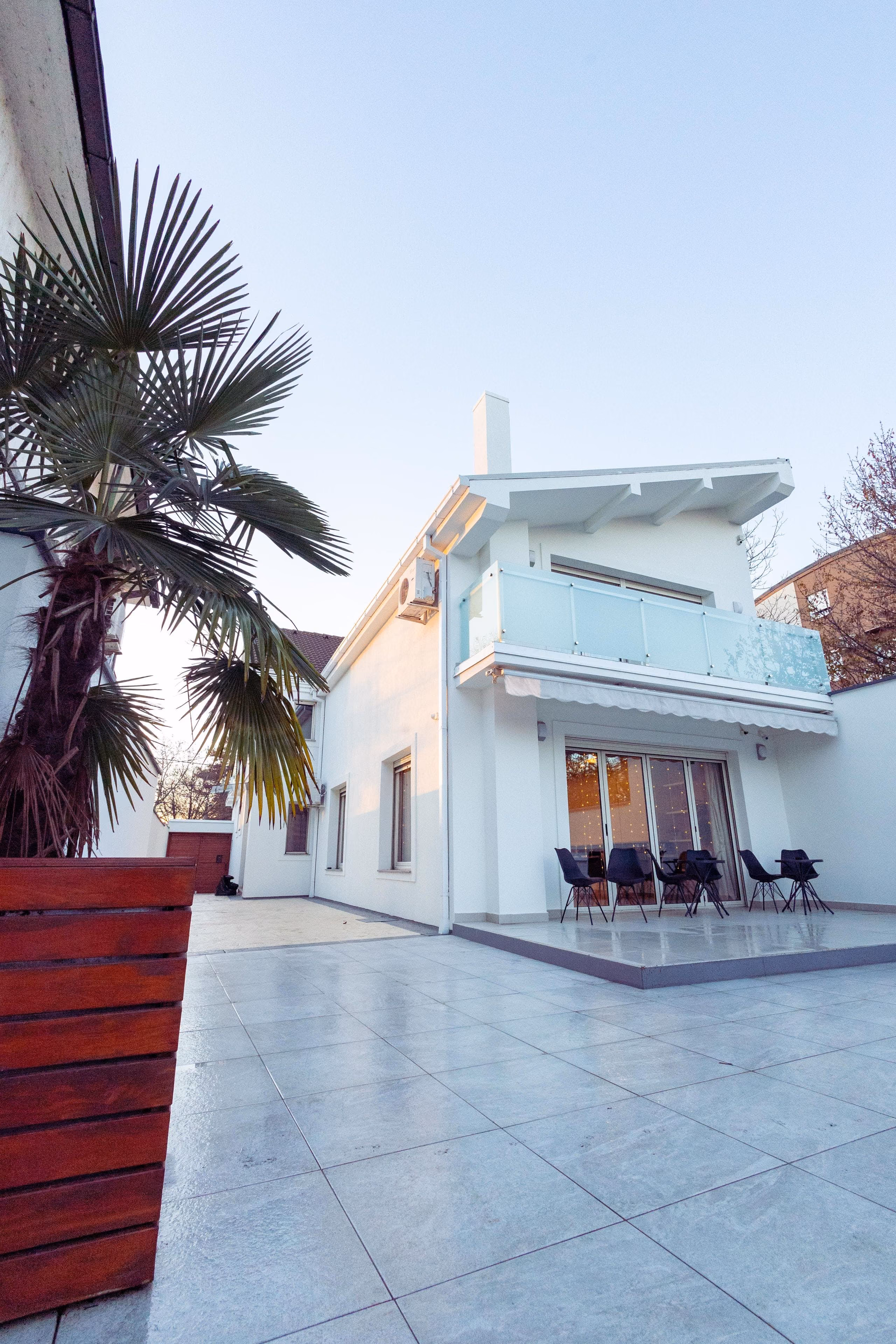 White rendered house with glass balcony, palm tree and tiled terrace in sunshine