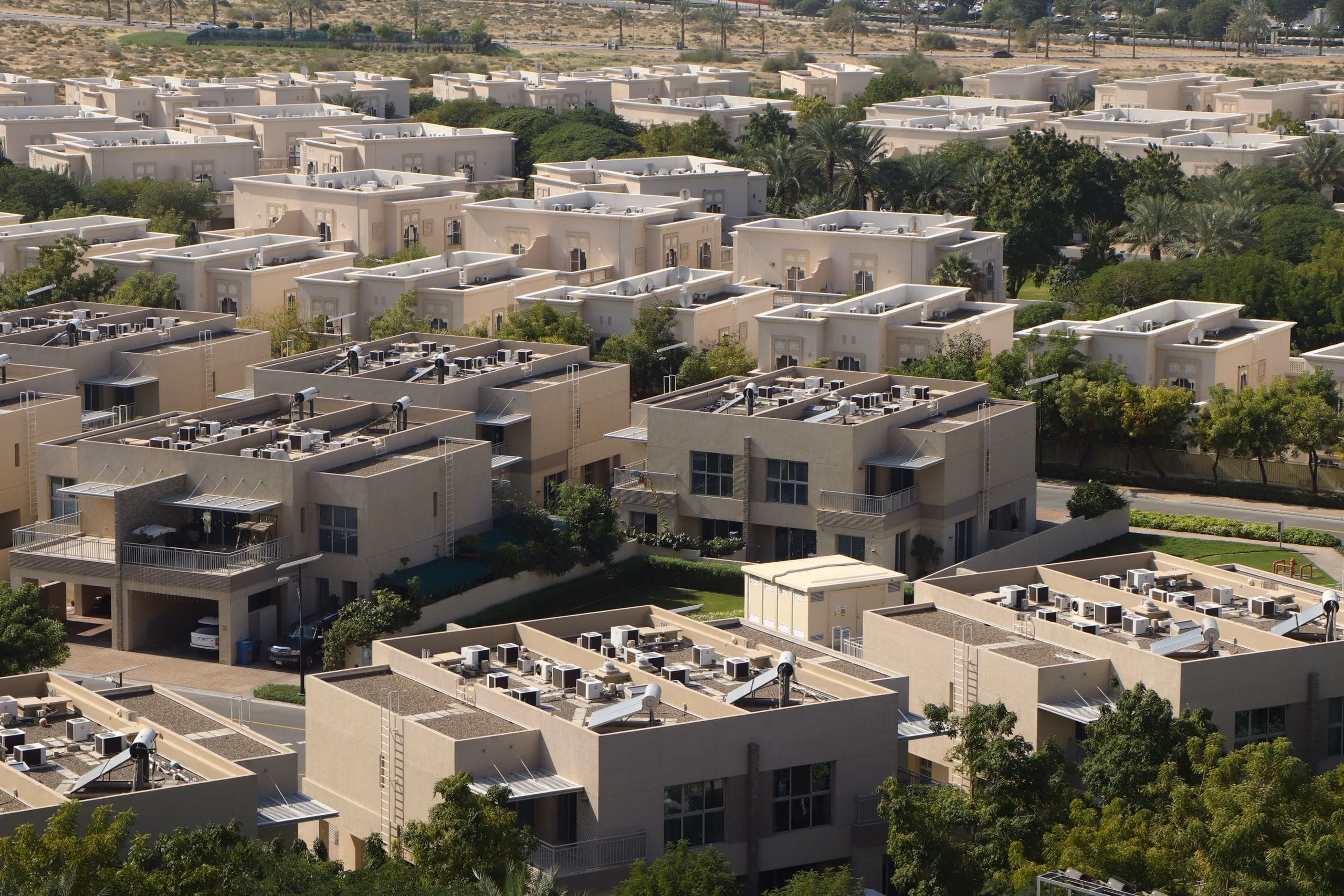 Aerial view of villa community with flat roofs, rooftop units and green landscaping