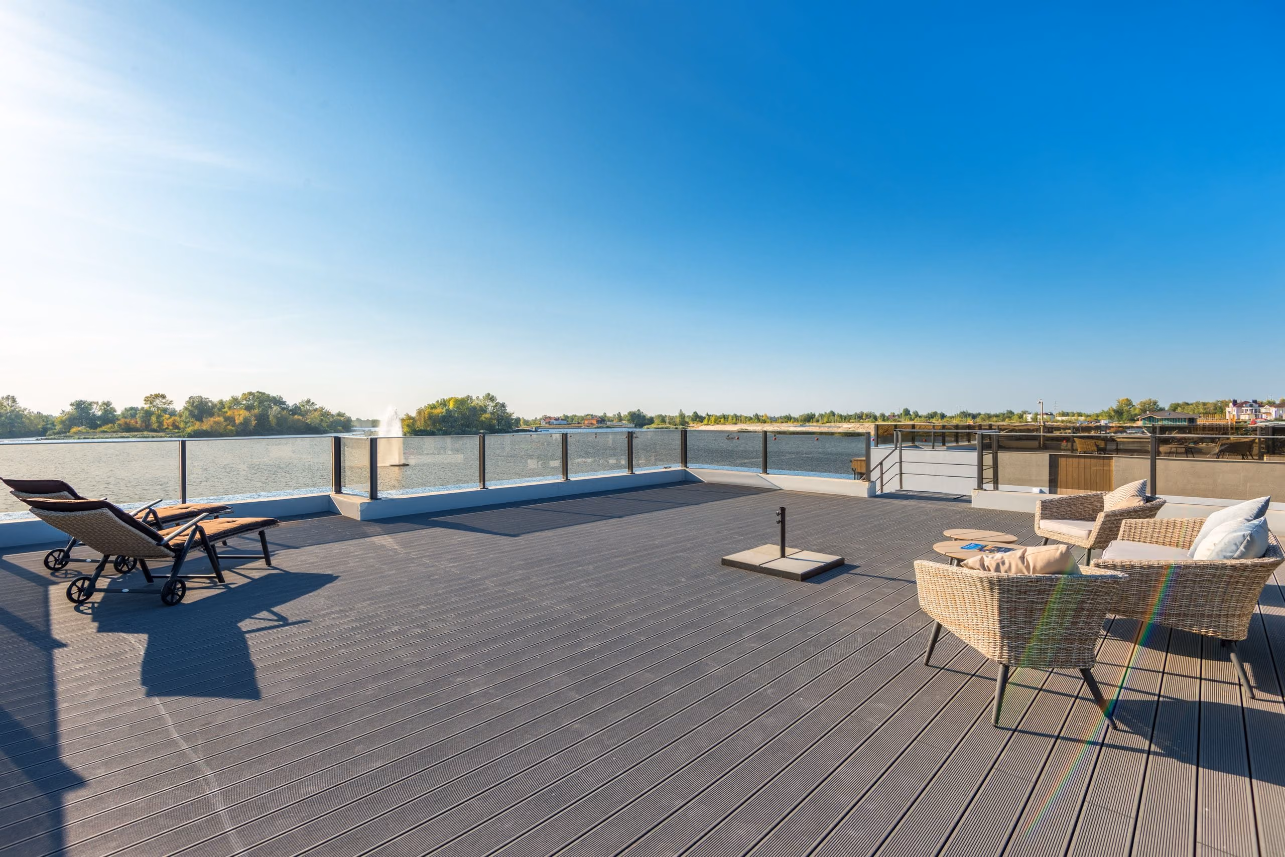Large open roof terrace with glass railing, sun loungers and wicker seating