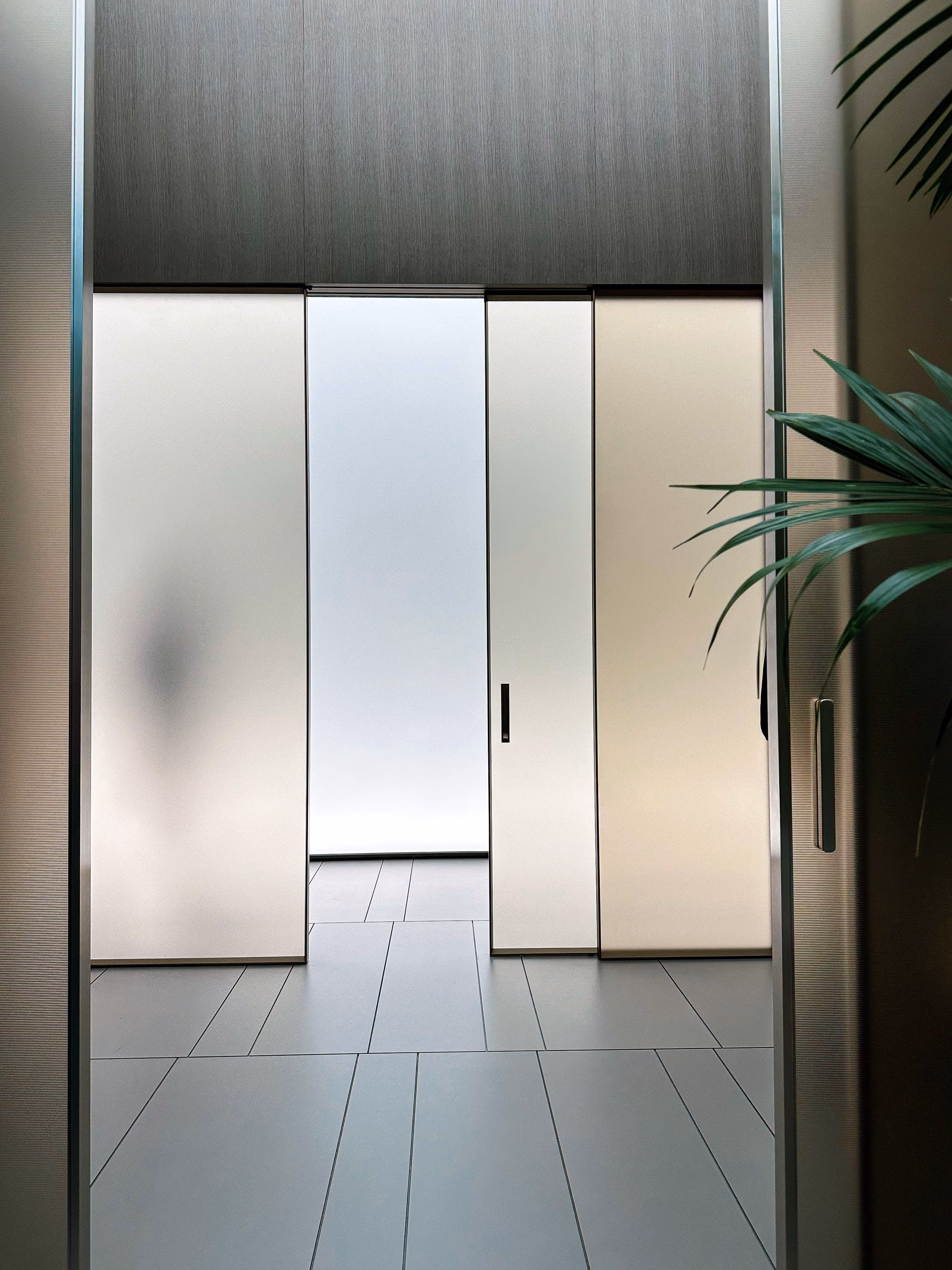 Frosted glass sliding doors in a slim frame along a calm, minimal corridor