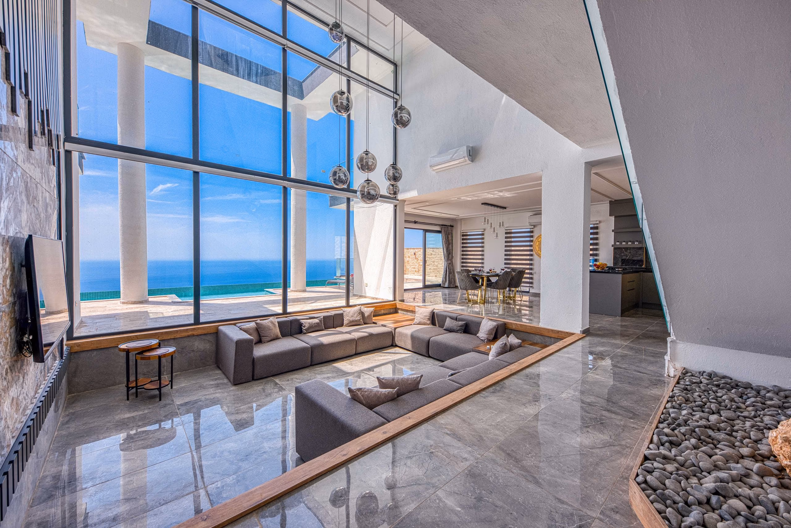 Glossy grey marble floor reflecting tall windows and pendant lights in a sunken lounge