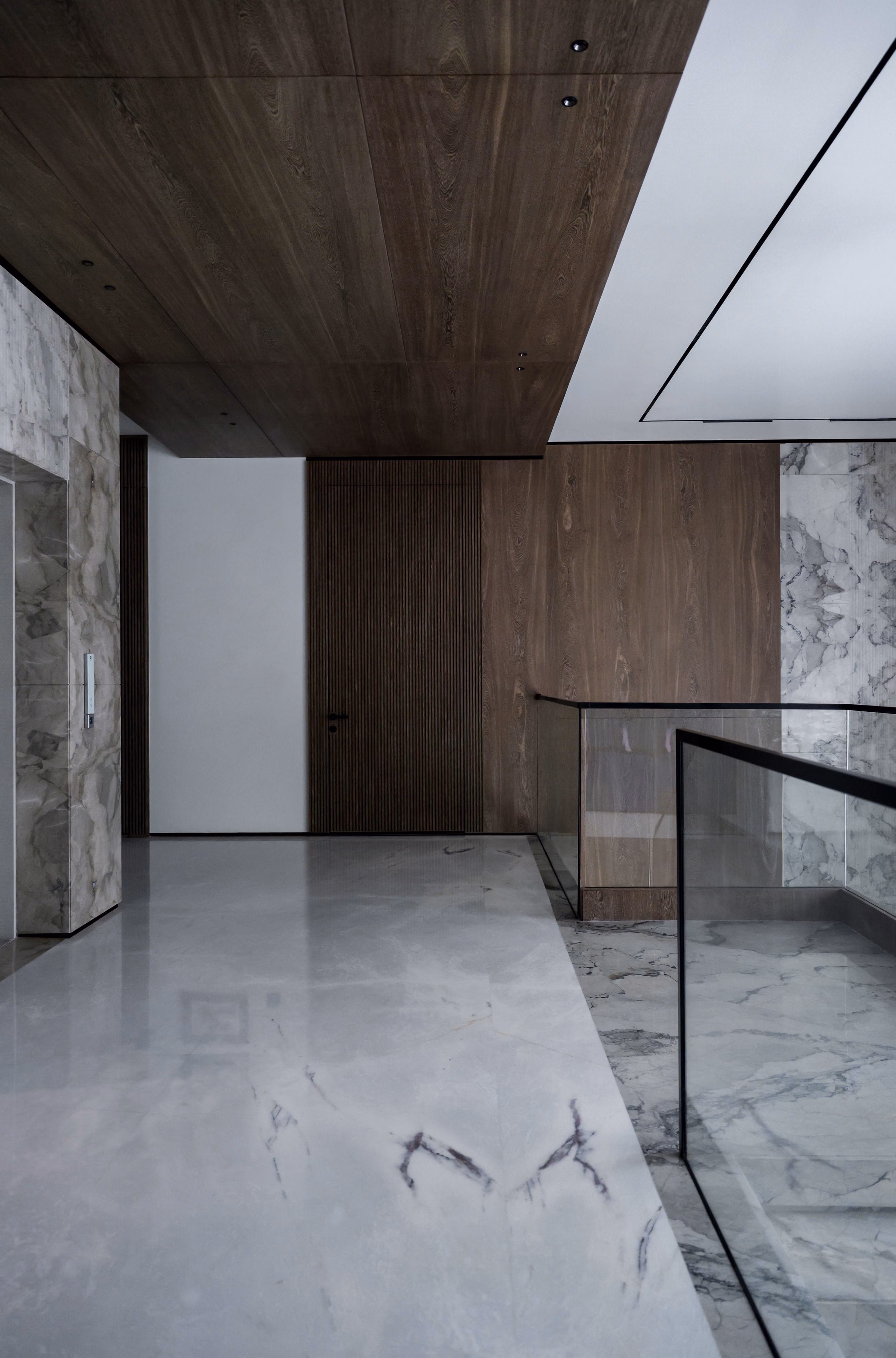 Polished grey marble landing with glass balustrade, walnut wall panels and a wood ceiling