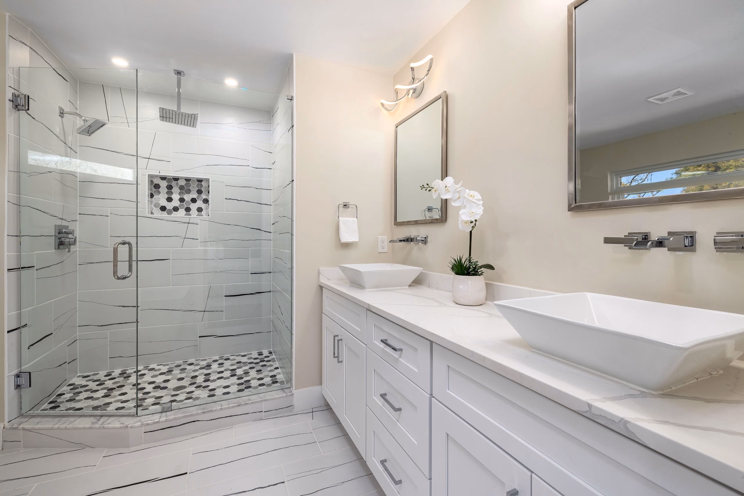 Bright bathroom with large-format tiles, frameless glass shower and long white double vanity