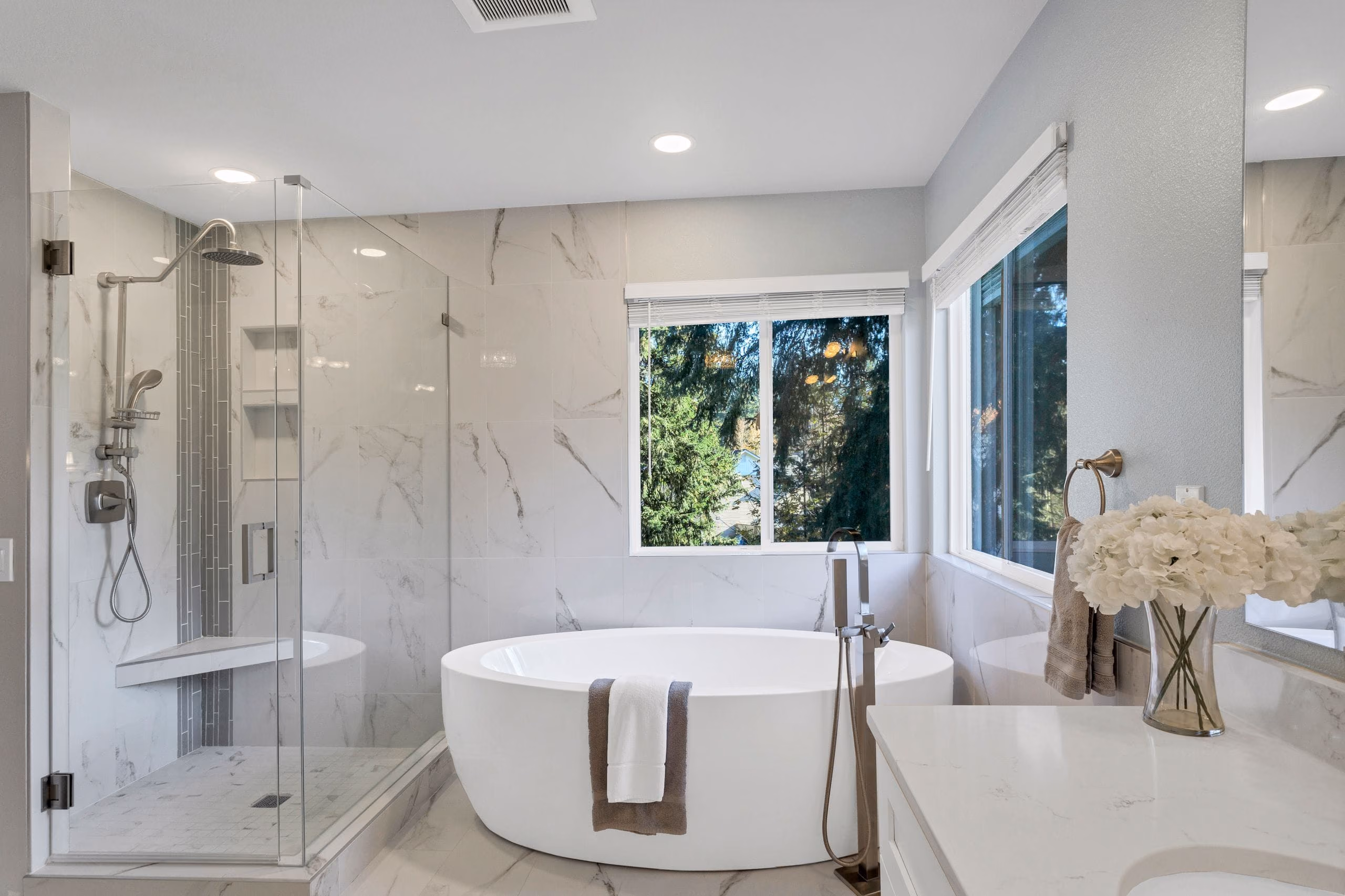 Marble-look tiled bathroom with freestanding bathtub, glass shower enclosure and garden window