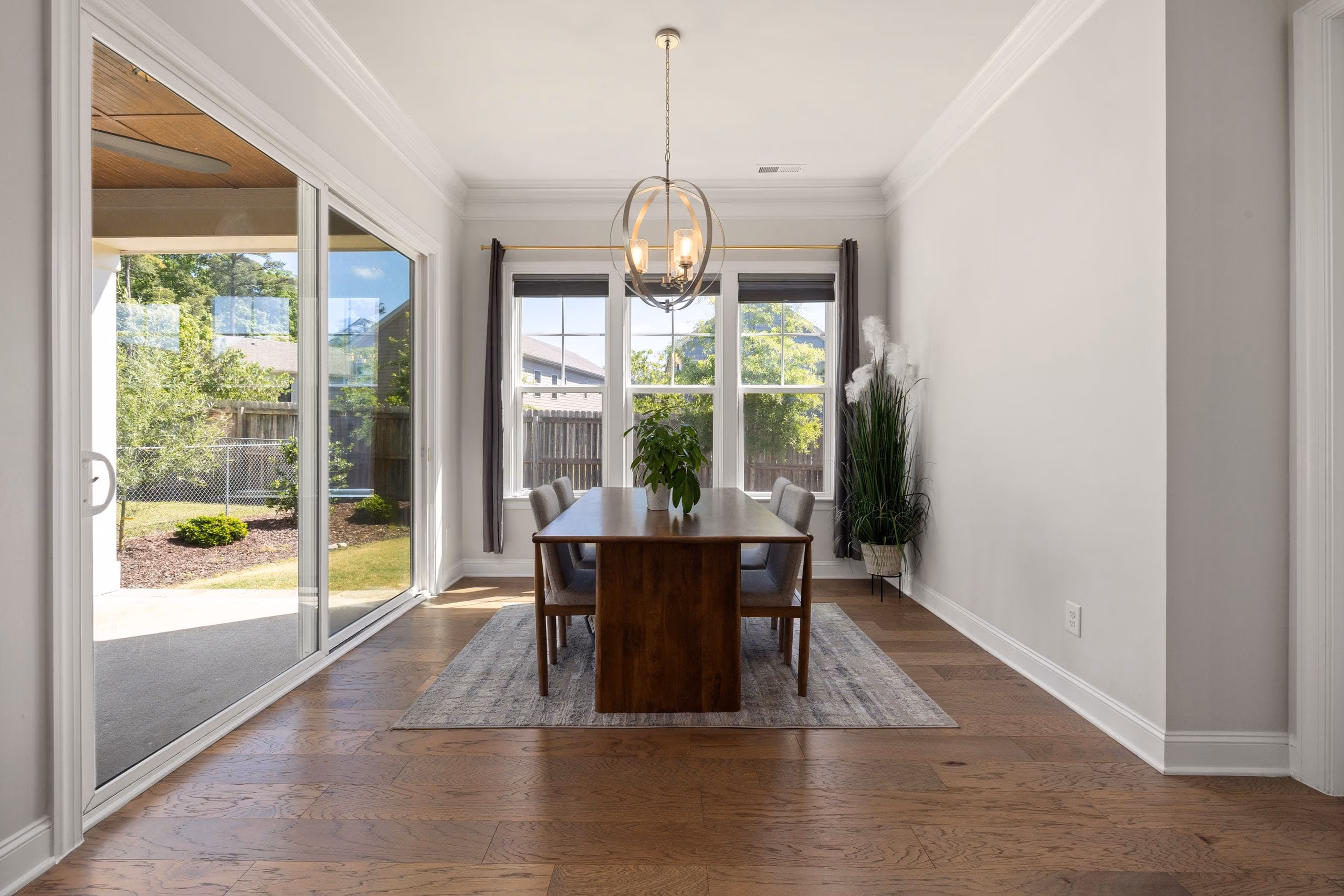 Light dining room with pendant chandelier, crown moulding, wood floor and sliding glass doors