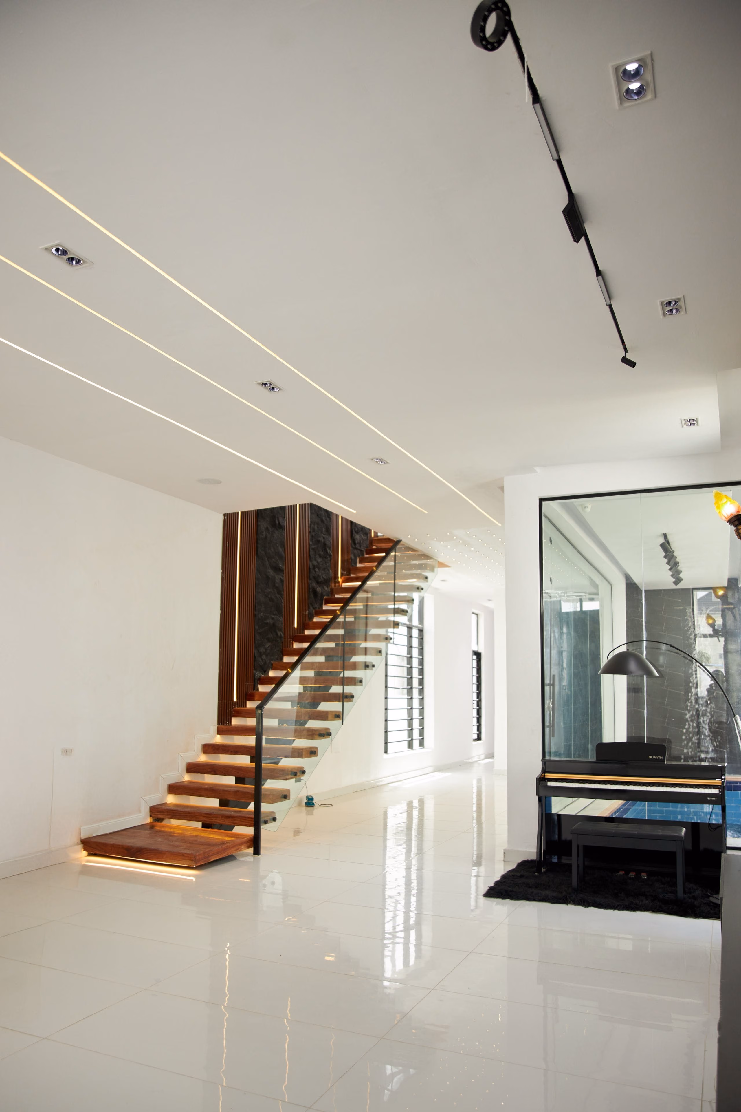 Minimal white hallway with floating wooden stairs, linear ceiling lights and polished floor