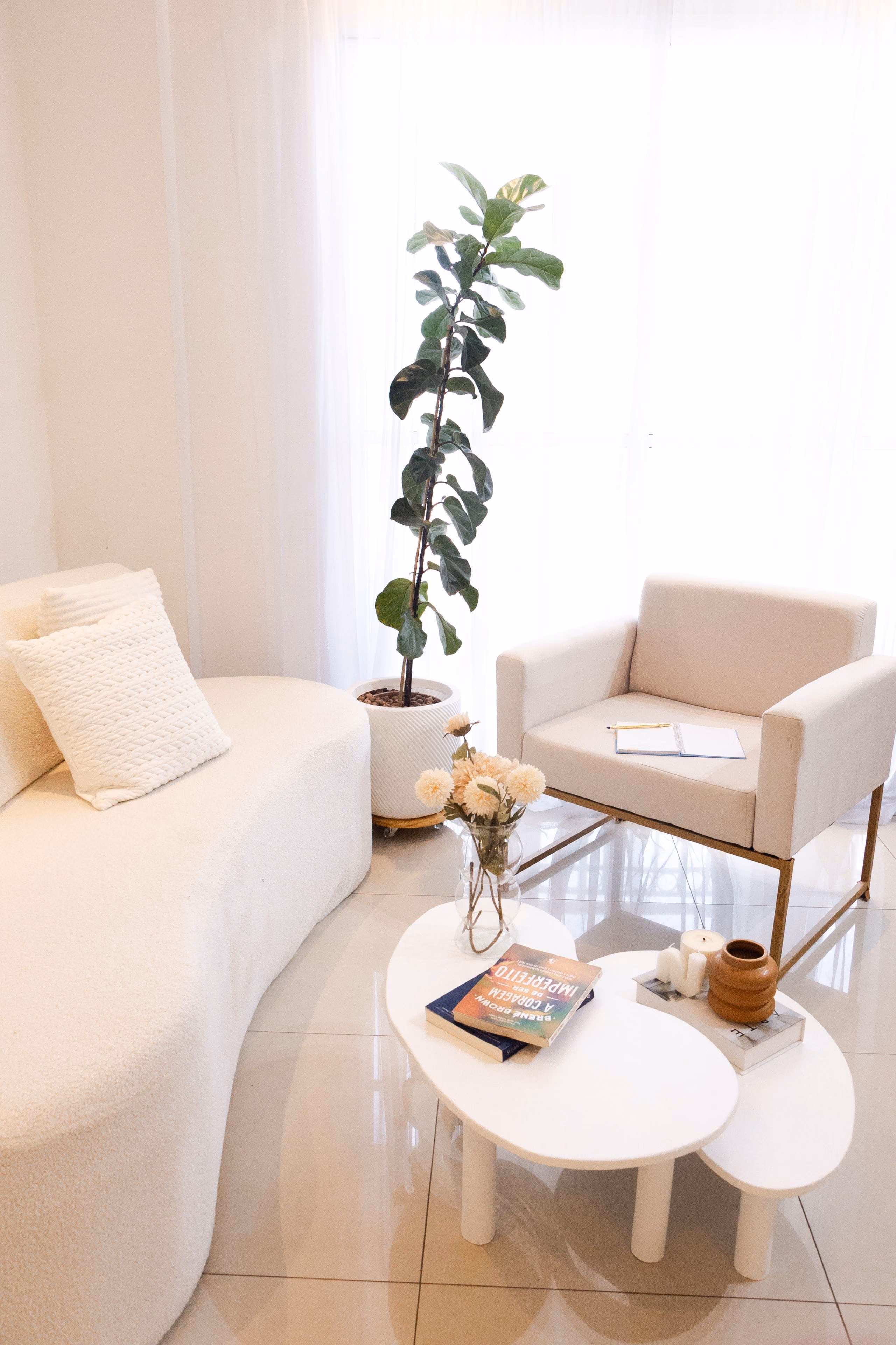 Light-filled corner with clean white walls, curved sofa, armchair and fiddle-leaf plant