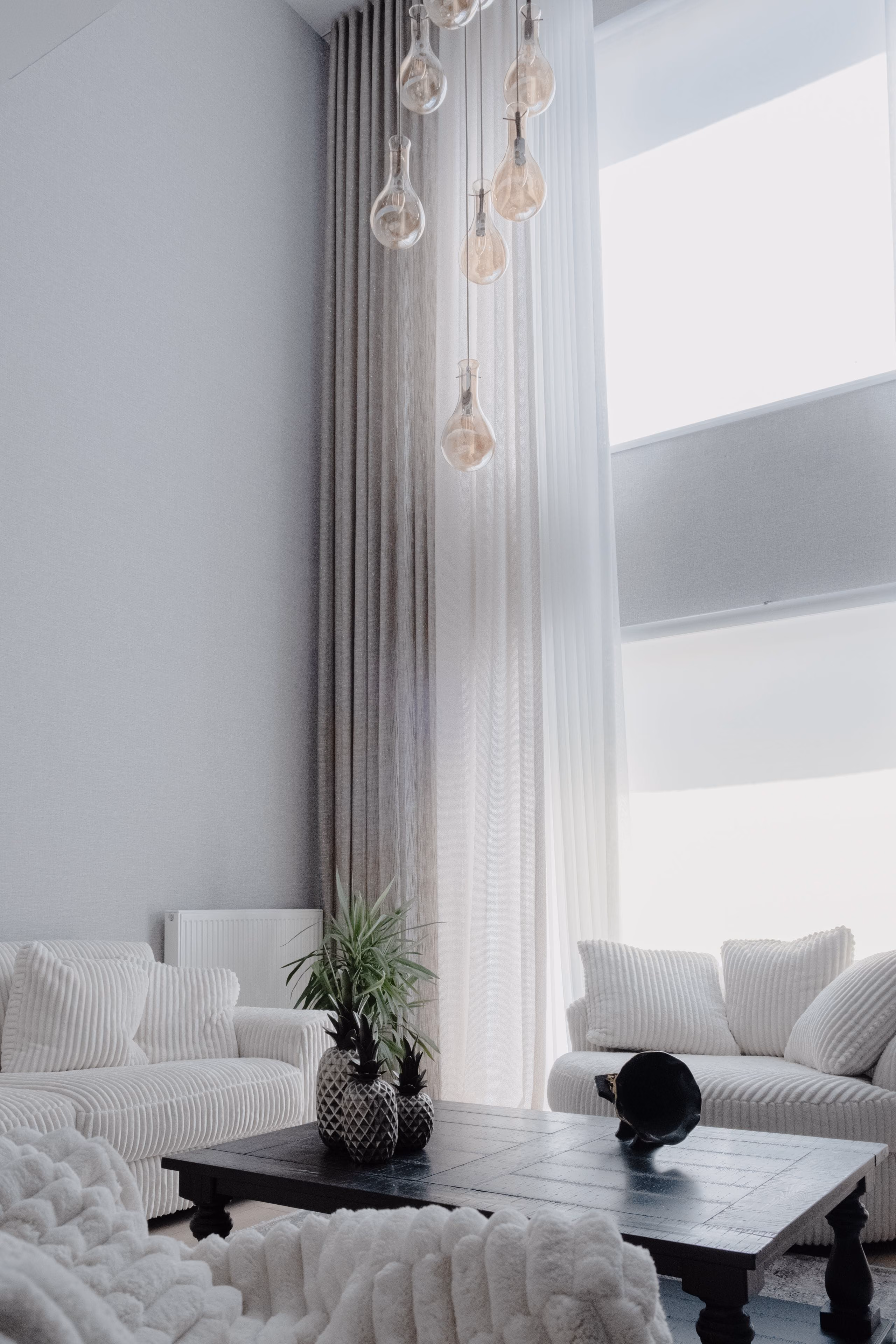 Double-height living room with pale painted walls, tall sheer curtains and white sofas