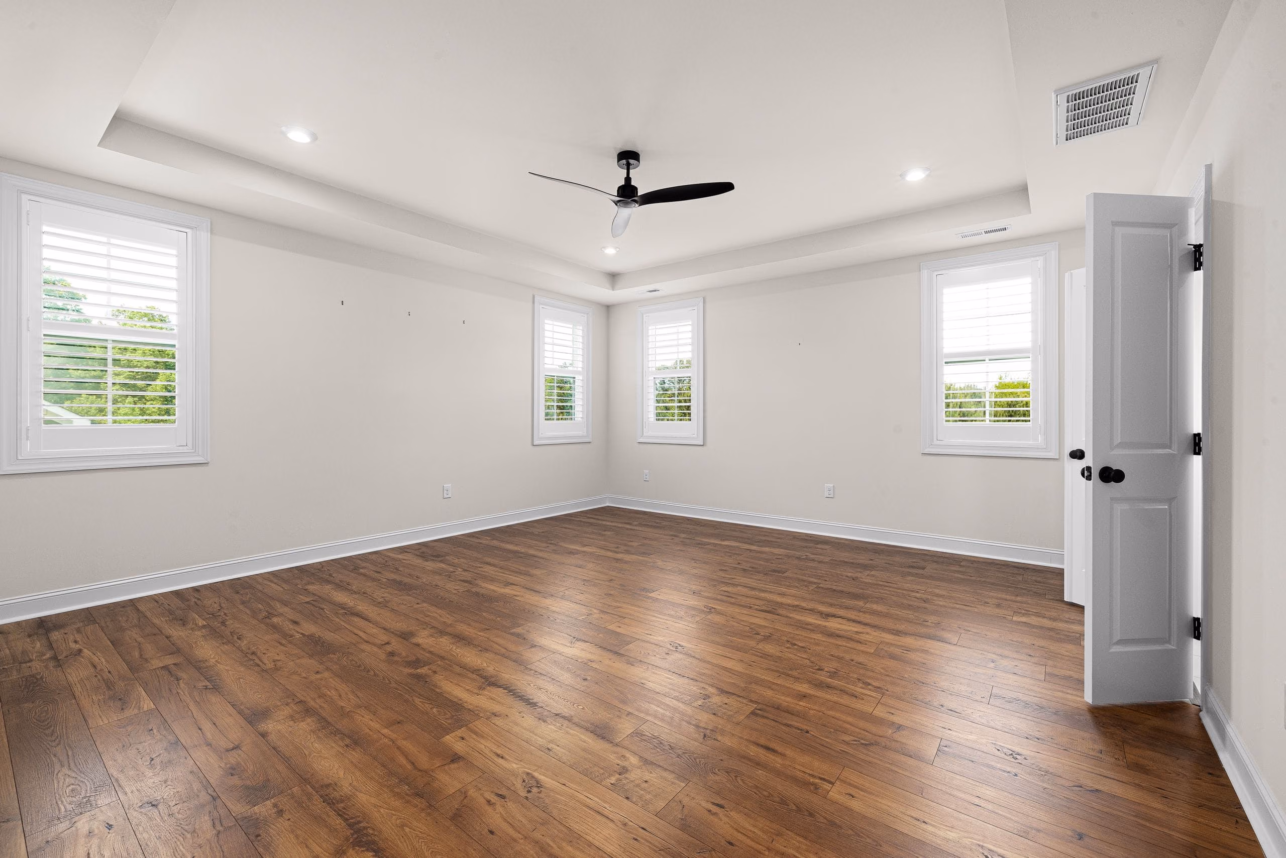Empty bright room with freshly painted walls, tray ceiling, ceiling fan and wood floor