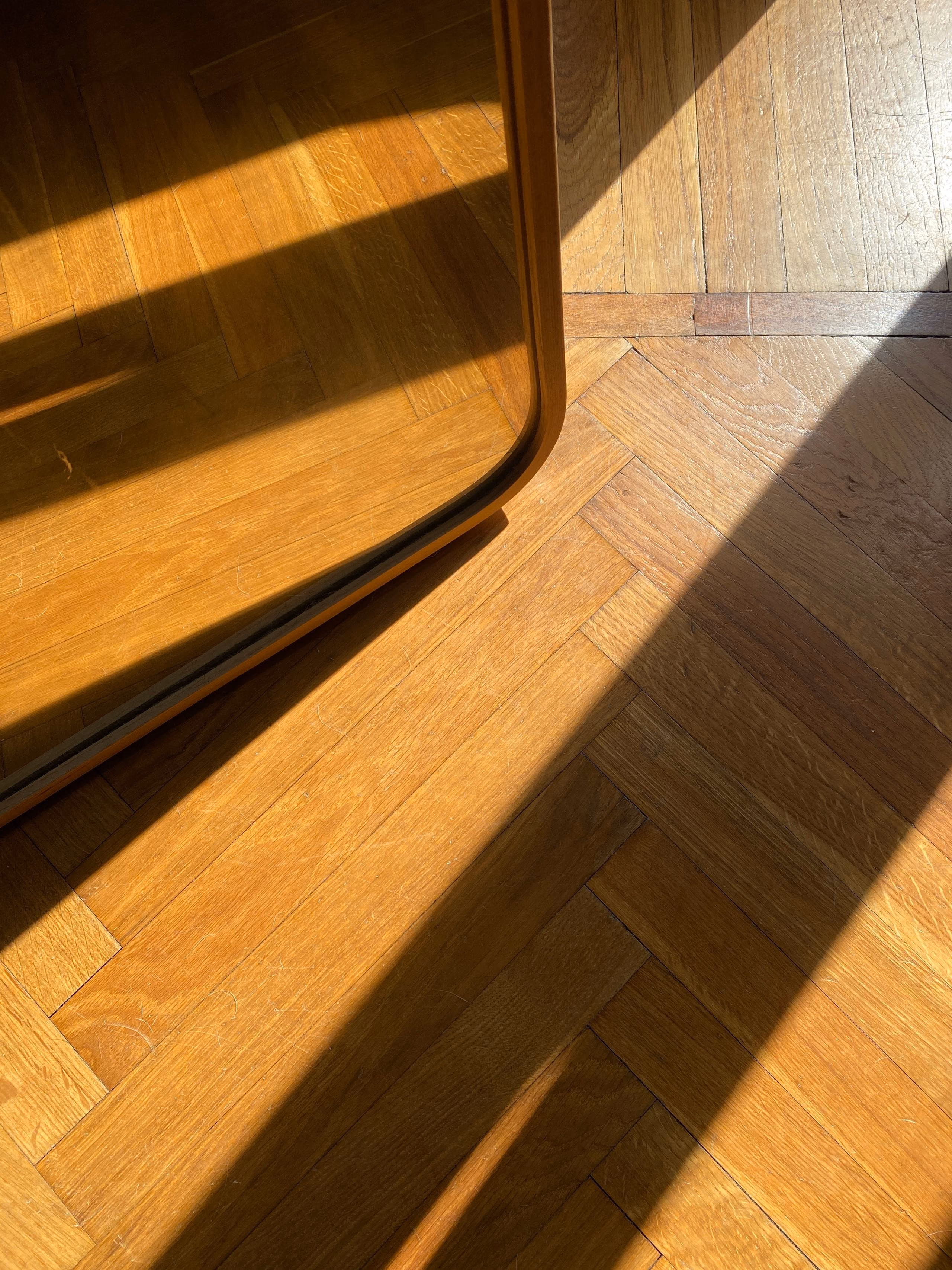 Sunlight and shadows falling across oak herringbone parquet beside a floor mirror