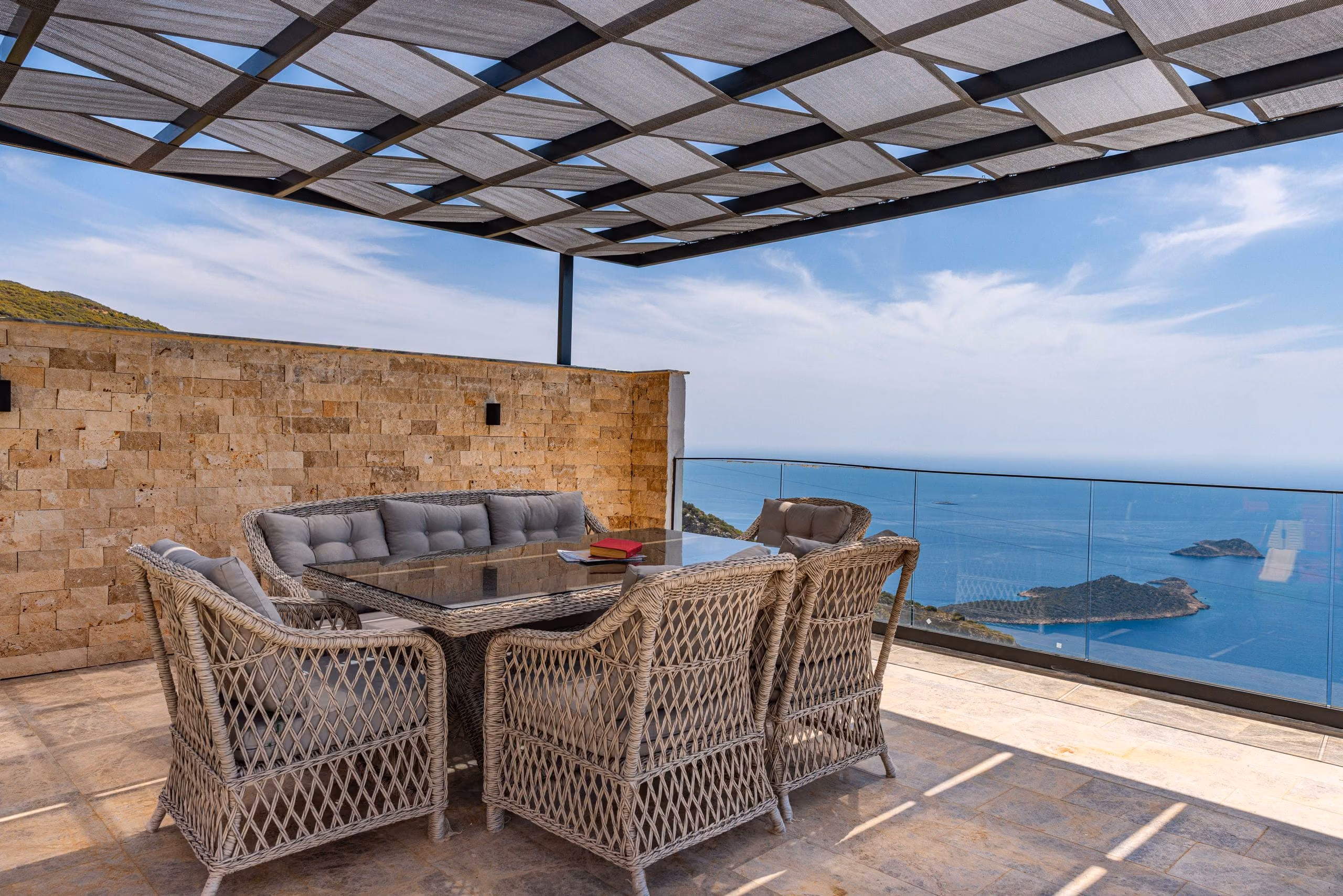 Covered stone-tiled terrace with wicker dining set and a glass balustrade overlooking the sea
