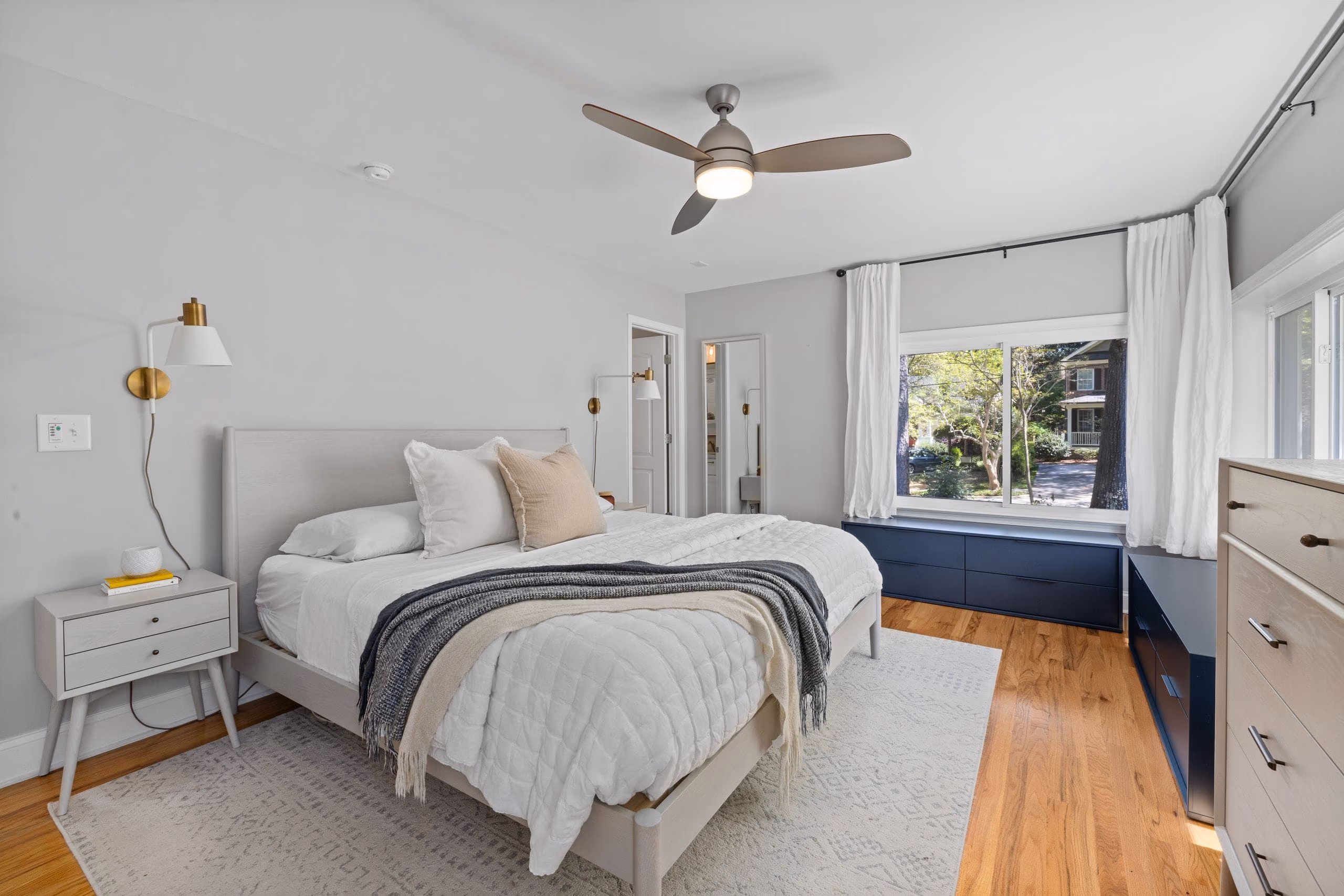 Freshly painted light grey bedroom with wooden floor, upholstered bed and ceiling fan