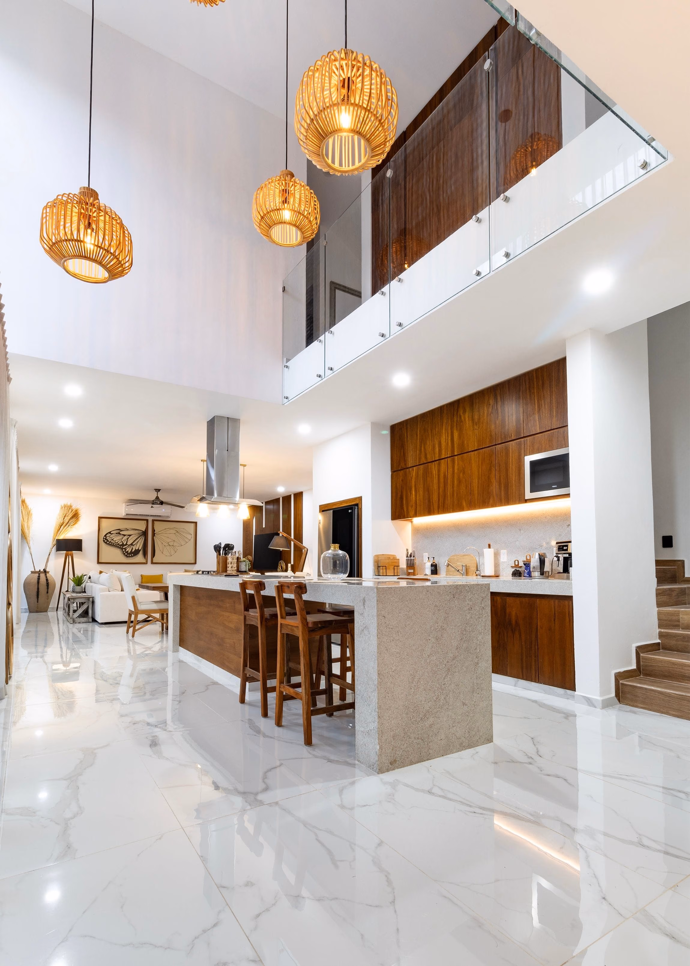Double-height kitchen with stone island, bar stools, wood cabinetry and marble floor