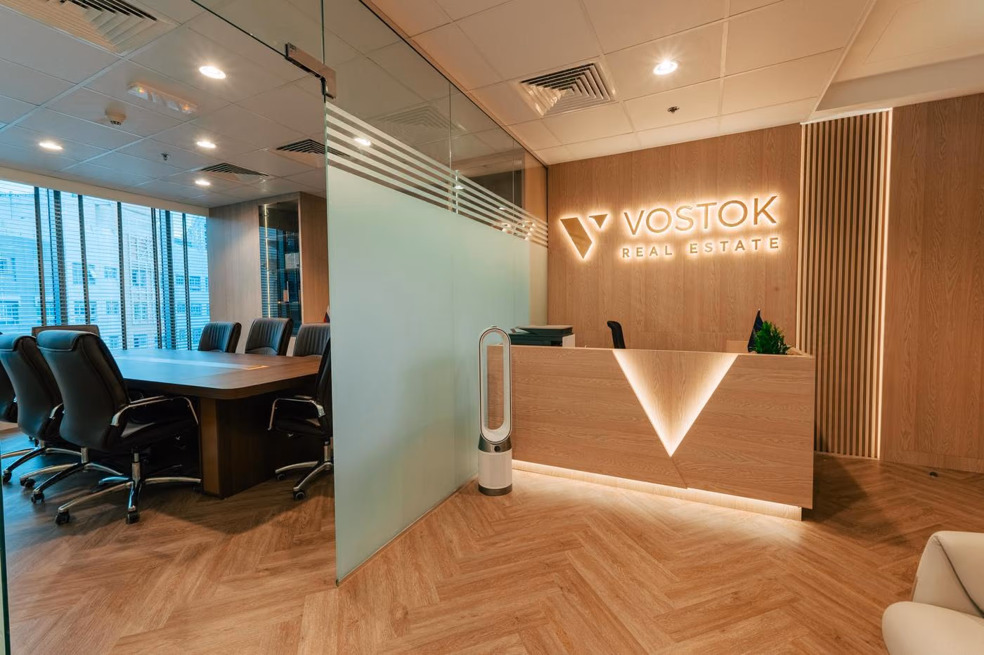 Yoritilgan logotip va geometrik shakldagi qabulxona stoliga ega Vostok Real Estate qabulxonasi